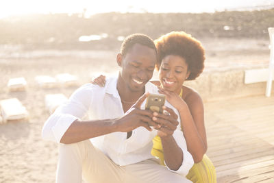 Couple using mobile phone while sitting at beach
