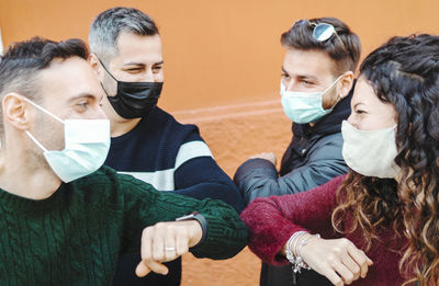 Cheerful friends wearing mask doing elbow bump while standing outdoors