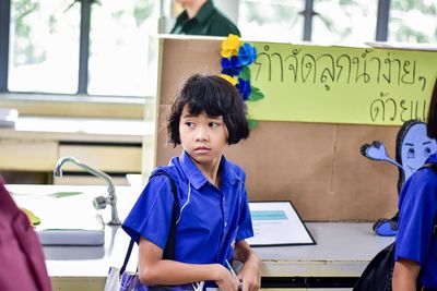 Girl looking away while standing by table in school