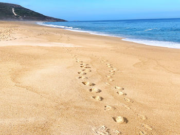 Footprints on sand at beach against sky