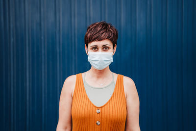 Portrait of young woman standing against blue wall