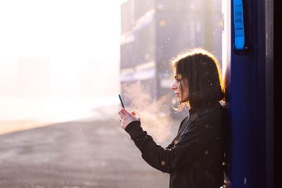 Side view of woman using mobile phone by cargo container