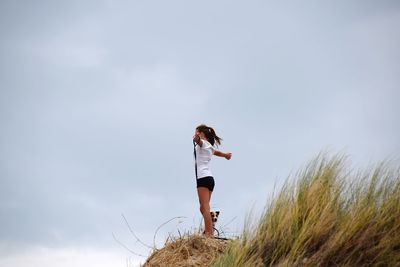 Side view of young woman with dog standing on rock at beach against sky