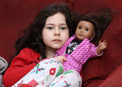 Beautiful young girl playing with her favorite doll on the couch