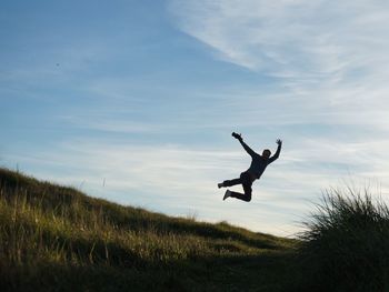 Man jumping over grassy field against sky