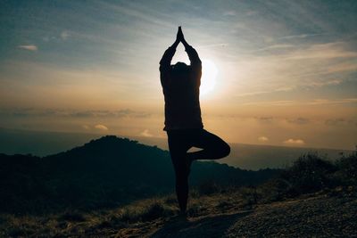 Silhouette man exercising in tree pose on mountain against sky during sunset