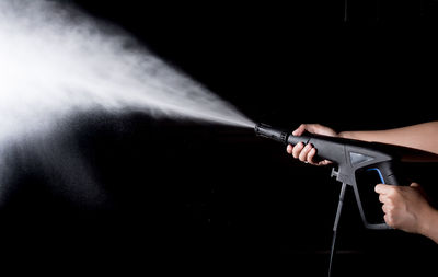 Cropped hand holding jet spray against black background