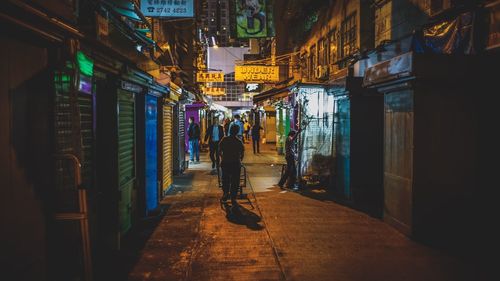 Rear view of man walking on illuminated street at night