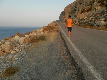 Rear view of woman walking on rock by sea