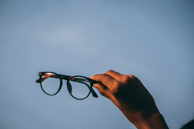 Close-up of hand holding eyeglasses against sky