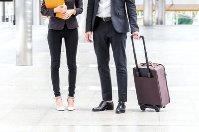 Low section of businesswoman standing by colleague holding luggage on footpath