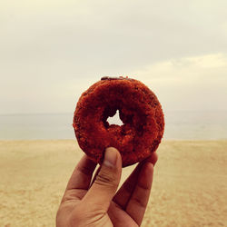 Close-up of hand holding a piece of donut on the beach