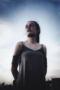 Low angle view of young woman standing against sky