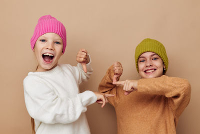 Portrait of smiling sisters wearing knit hat against beige background