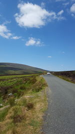 Empty road amidst field against sky