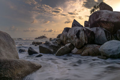 Rocks on beach against sky during sunset