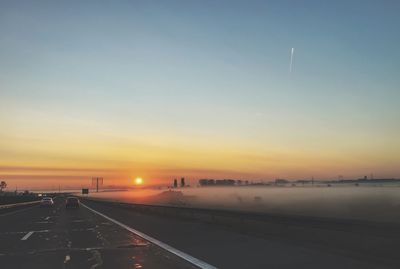 Road by city against sky during sunset