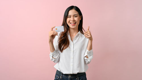Portrait of young woman standing against pink background