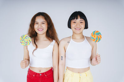 Portrait of smiling lesbian couple holding lollipop against gray background
