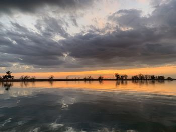 Scenic view of lake against dramatic sky during sunset