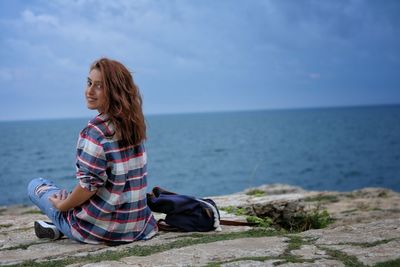 Woman sitting on beach against sky