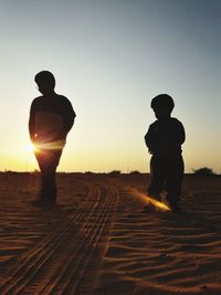 Silhouette boys standing on land against clear sky during sunset