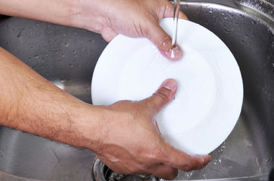 Cropped image of hands cleaning plate in kitchen sink