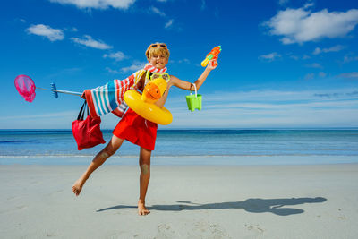 Rear view of woman with arms outstretched standing at beach against sky