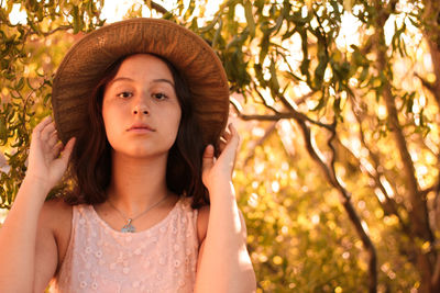 Portrait of beautiful young woman standing against tree