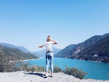 Rear view of woman standing at lake against blue sky