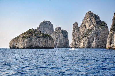 Rocks in sea against clear blue sky