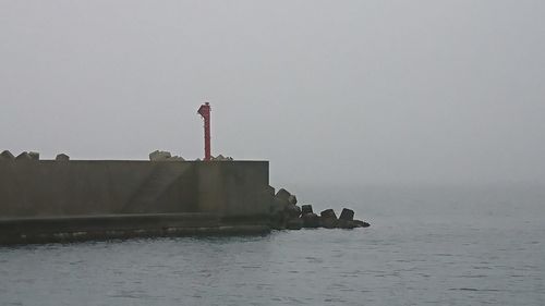 Lighthouse by sea against clear sky