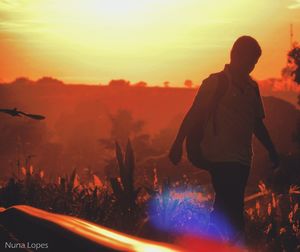 Silhouette man with arms raised against sky during sunset