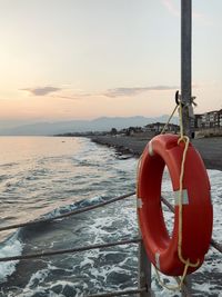 View of lifebuoy on a pier post in sea against sky during sunset