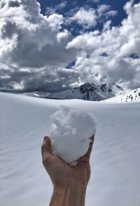 Close-up of person holding snow on against sky