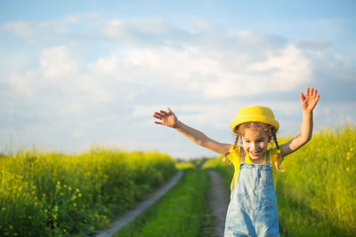 Young woman with arms raised standing on field against sky