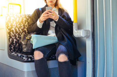 Midsection of woman using phone while traveling in train