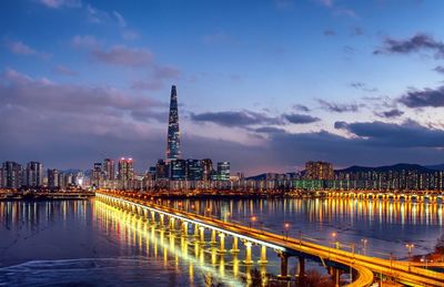 Illuminated buildings by river against sky at night