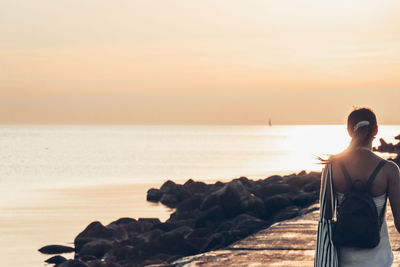 Rear view of woman looking at sea against sky during sunset