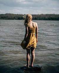 Rear view of young woman standing on rock by lake