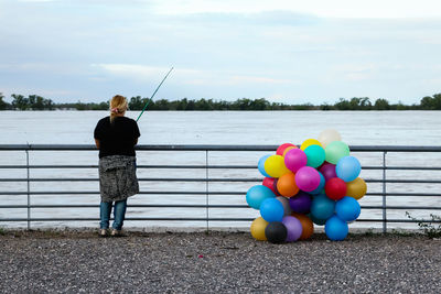 Full length rear view of woman fishing in lake by colorful helium balloons