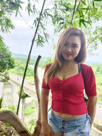 Portrait of smiling young woman standing against trees