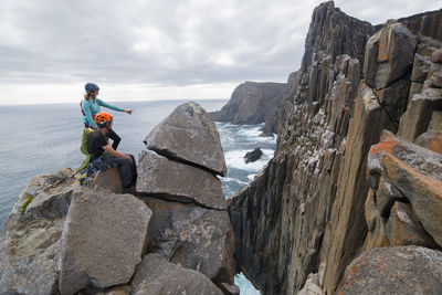 People on rocks by mountain against sky