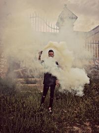 Portrait of young woman with distress flare emitting smoke on field