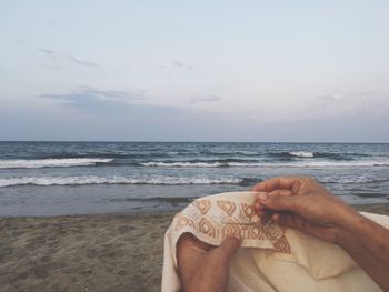 Midsection of man holding sand at beach against sky