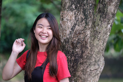 Portrait of smiling young woman against tree trunk