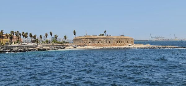 Building by sea against clear blue sky