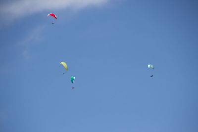 Low angle view of people paragliding against clear blue sky