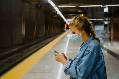 Side view of female texting on cellphone while waiting for arriving train in station