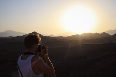 Rear view of woman photographing at sunset